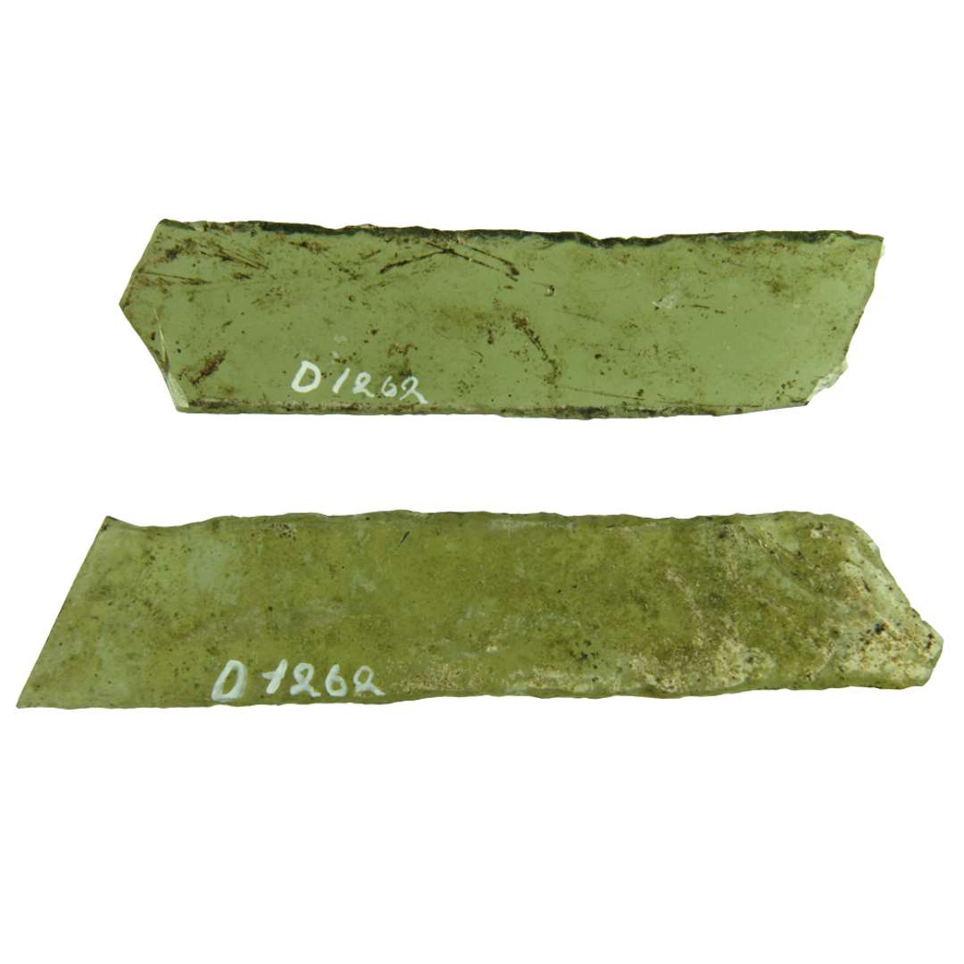 2 fragmenterede ruder af klart grønligt glas med afnappede kanter, antagelig begge af form som langtrukket paralellogram. Den ene ende er afbrudt på den ene af ruderne.  Største mål henholdsvis: 2,25 x 9 cm. og 2,25 x 10,5 cm.