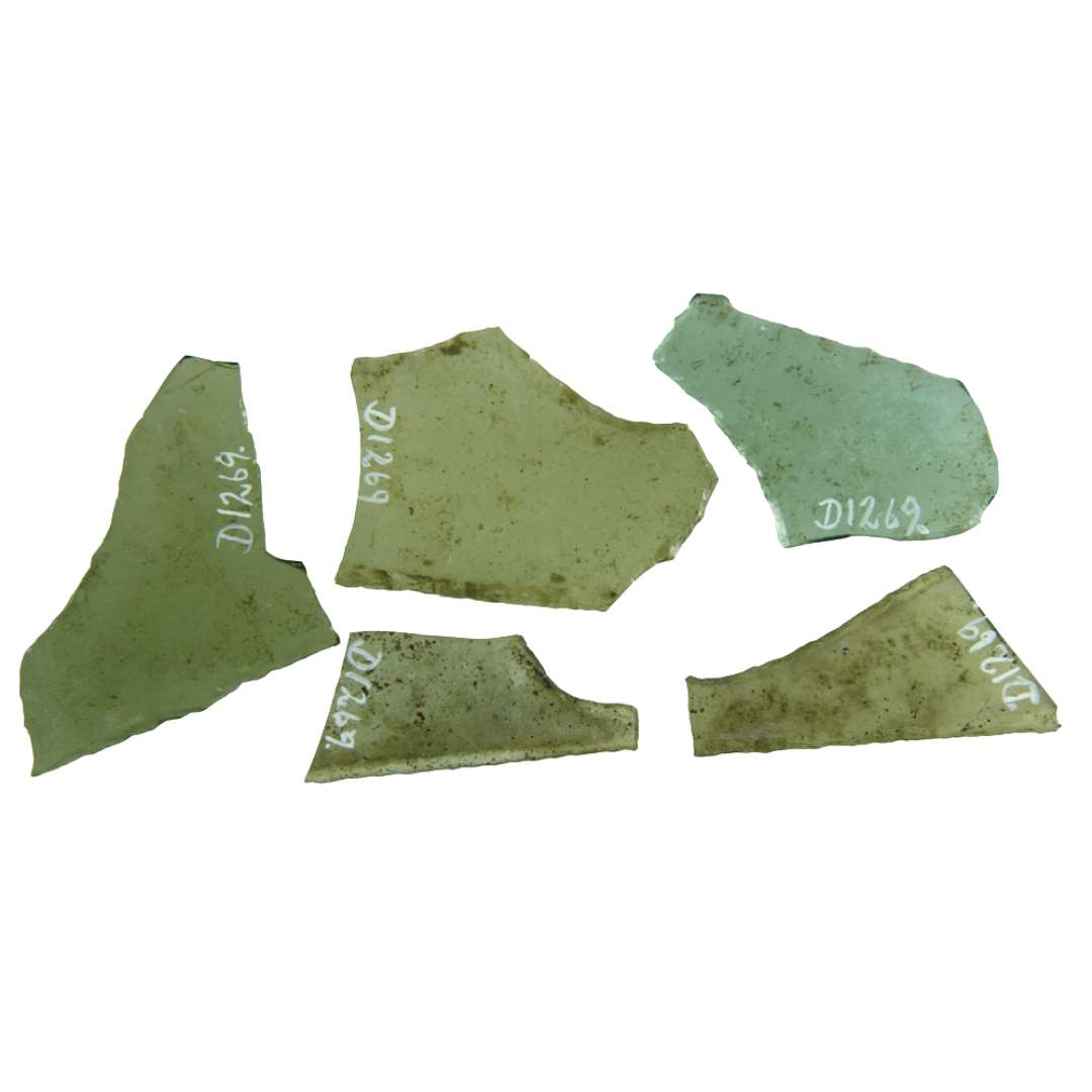 5 rudefragmenter af klart grønligt glas med afnappede kanter. Fragmenterne hidrører antagelig alle fra ruder af trapezagtige former med konkave indsvingninger og en næbeagtig udtunget spids i den ene side.