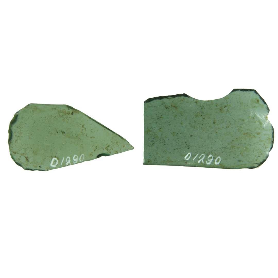 2 fragmenter af klart grønligt glas med afnappede kanter. De hidrører fra ruder fra aflang form med deres ene side dannet af en natrurlig smelterand og med deres ene ende tungeformig afrundet. Største mål: 2,9 x 5,45 cm, og 3,45 x 5,6 cm.