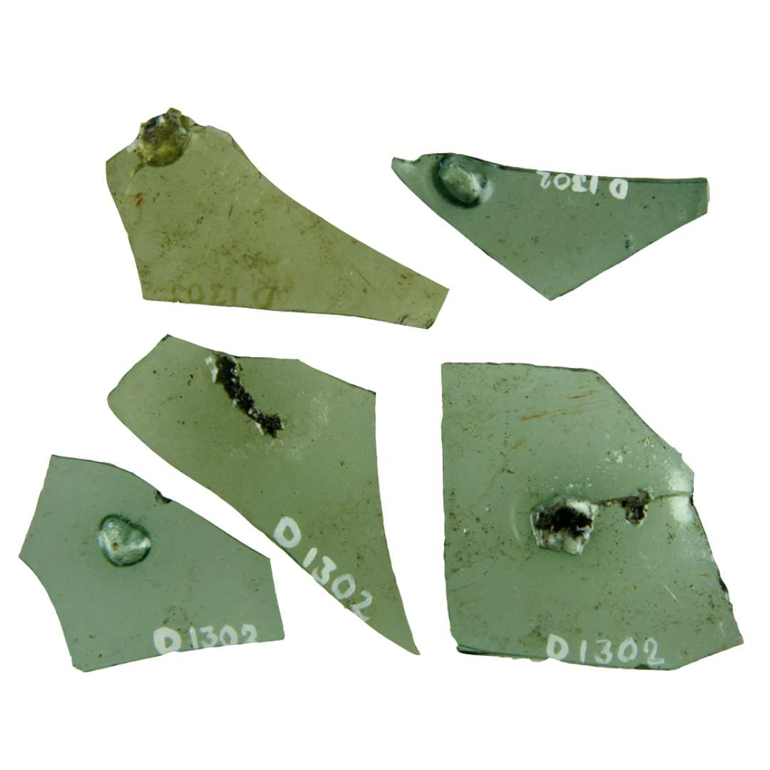 13 rand og midterskår af klart grønligt glas i hvis masse der sidder indkapslet urenheder i form af ærtestore kvartsklumper. Et af skårene bærer afnapningsspor langs den ene kant. Dimension fra 1,8 x 22 cm. til 4,35 x 4,6 cm.