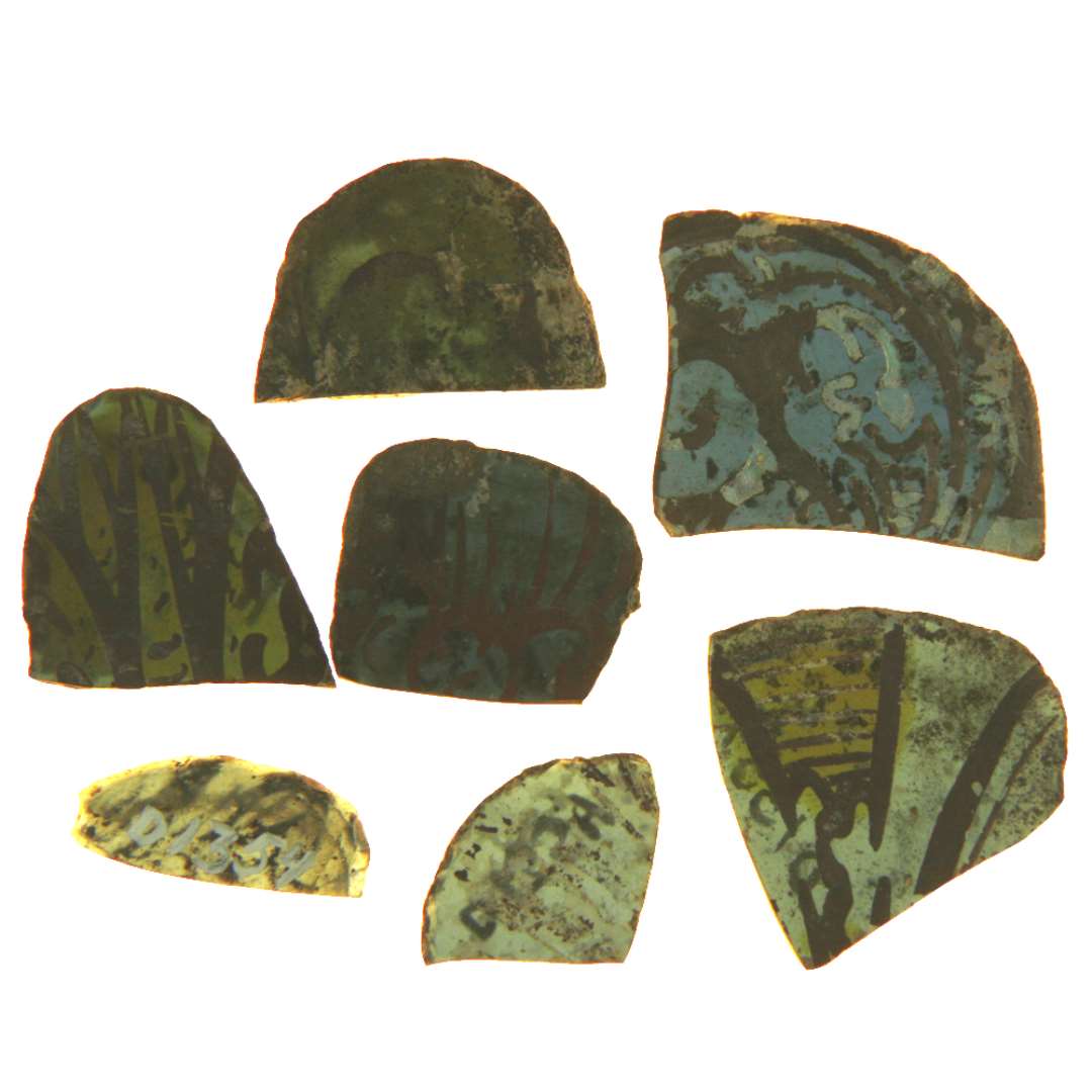 7 fragmenter af ruder af blåt glas med afnappede kanter bemalet med stiliserede plante og stregornamenter i brunlig farve, 2 skår viser tillige bemaling med gul farve. Hidrører antagelig fra ruder af forskellige tungeagtige former. Største diension ca.: 2,2 x 1,0 cm. - 1,6 x 1,6 cm. - 2,3 x 1,9 cm. - 2,5 x 2,2 cm. - 1,8 x 2,6 cm. - 2,55 x 2,55 cm. - 2,45 x 2,9 cm.