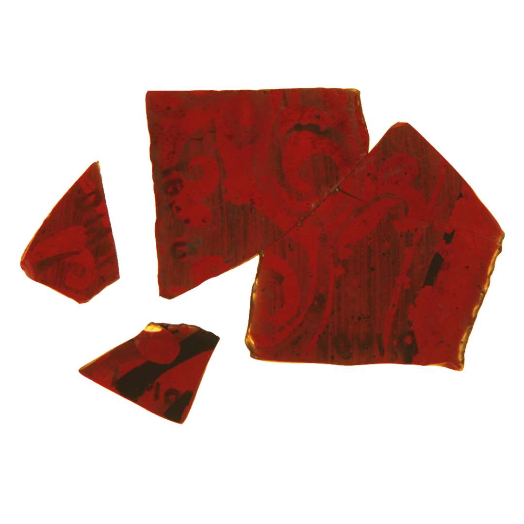 5 fragmenter, heraf 3 sammenlimede, af rødt glas dekoreret med et planterankemotiv dannet alene ved tynd, brunlig bemaling af baggrunden omkring ornamentet. Kun en stump af rudens afnappede yderkant er bevaret, således at rudeformen ikke lader sig erkende.  Den sammenlimede flades største mål: ca. 3,75 x 4,7 cm.