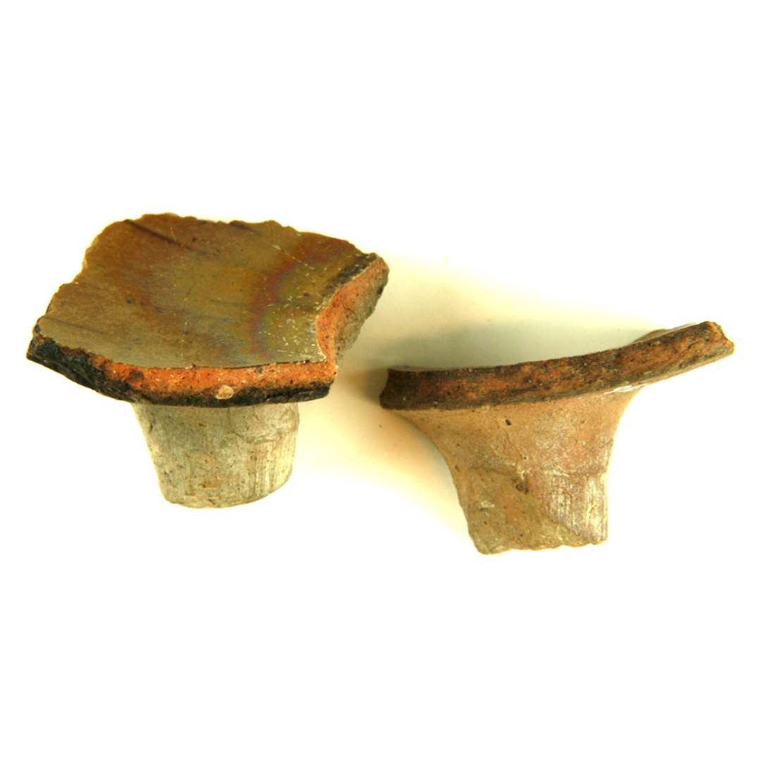 2 stumper lerkartæer (den ene fragmenteret) fra stjertpotte af rødbrunligt lergods, begge kar med blyglasur på den med tæerne sammenhørende karinderside.