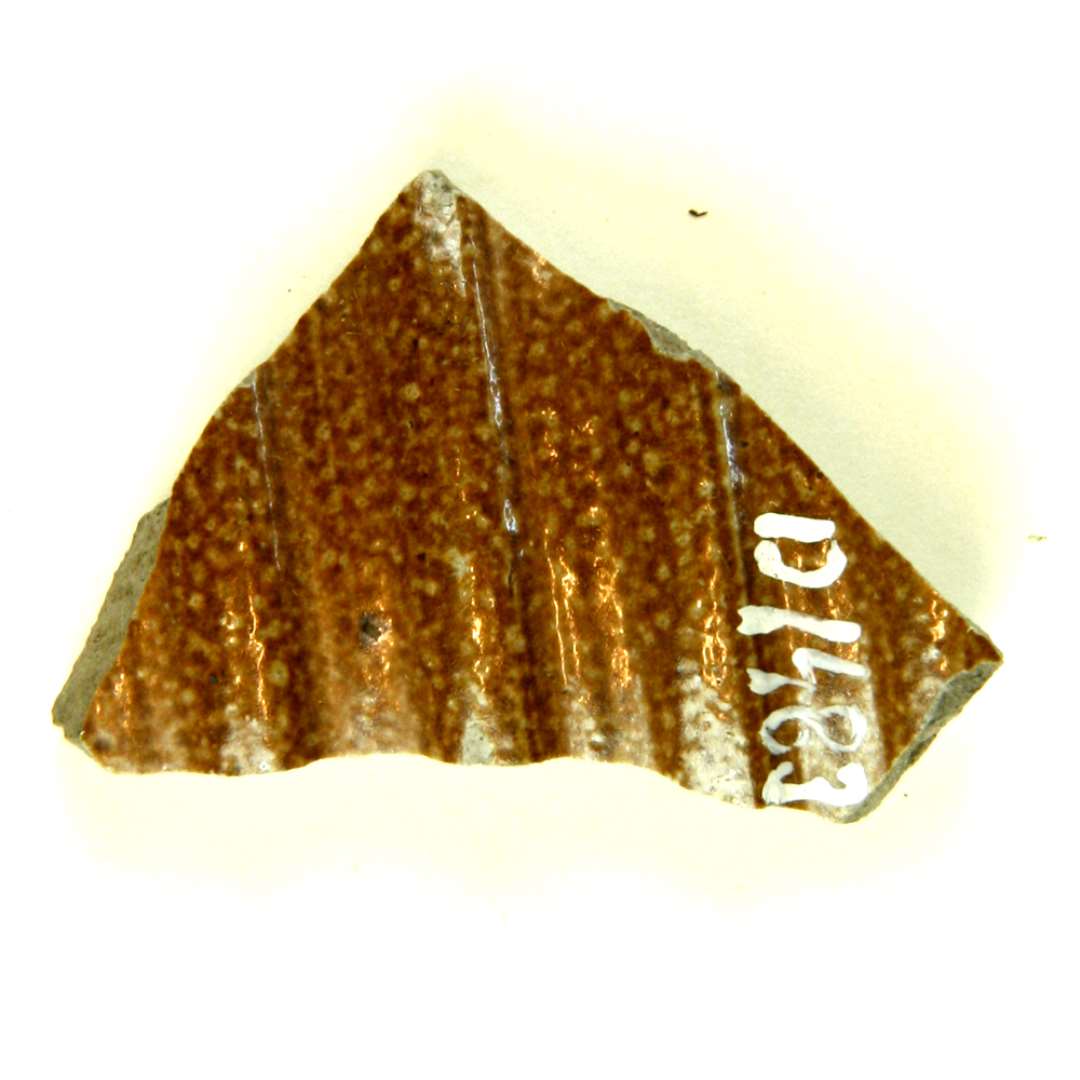 Halsskår af lysegråt stentøj med brun bemaling og saltglasur på ydersiden der fremtræder med kraftige vulster og furer, indersiden er kun dækket med saltglasur.