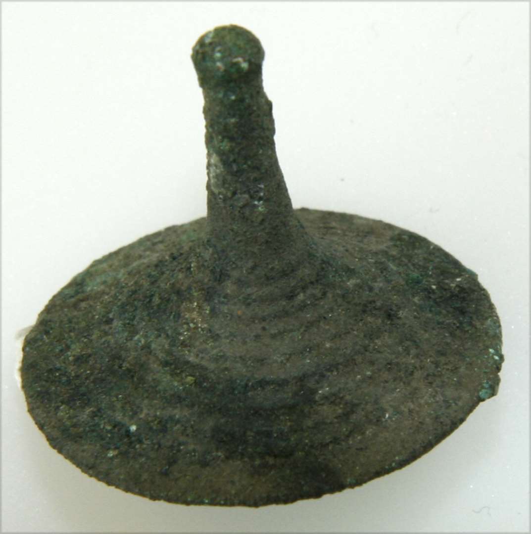 Tutulus af bronze. Med øsken på bagsiden. Dekoreret med koncentriske ringe. Højde: 2,5 cm., diameter: 2,7 cm.