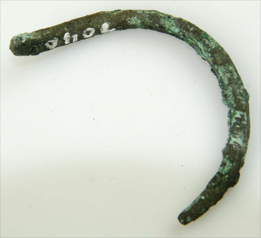 Fragment af håndledsring af bronze. Af bronzestang med cirkulært tværsnit. Fragmentets største mål: 6 cm.