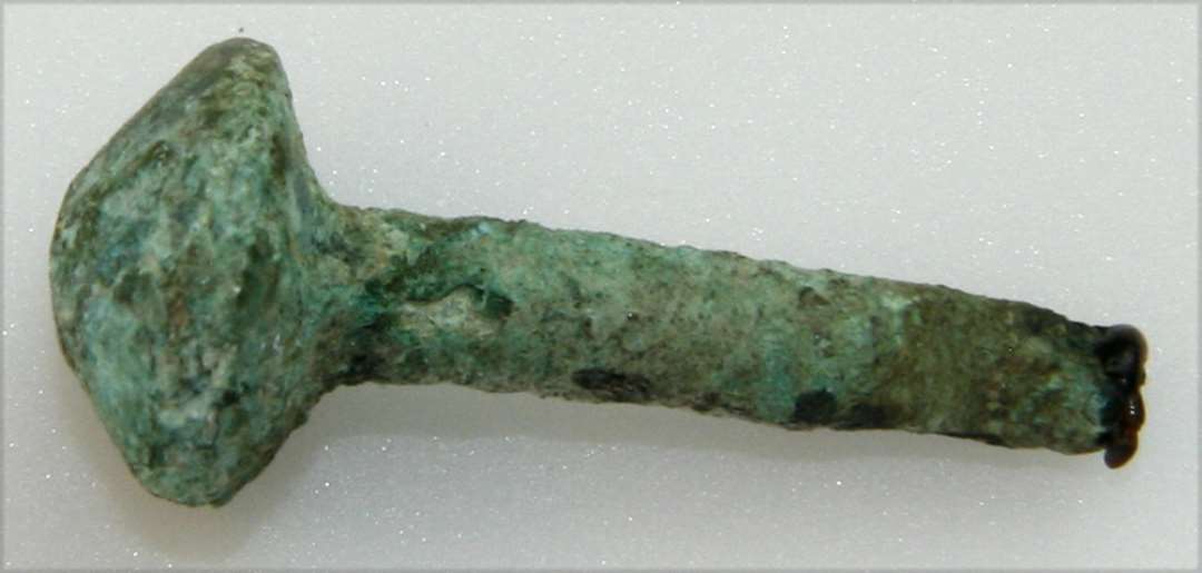 Fragment af bronzenål. Stilken afbrækket. Hovedet skiveformet, med hvælvet overside. Fragmentets længde: 2,7 cm.