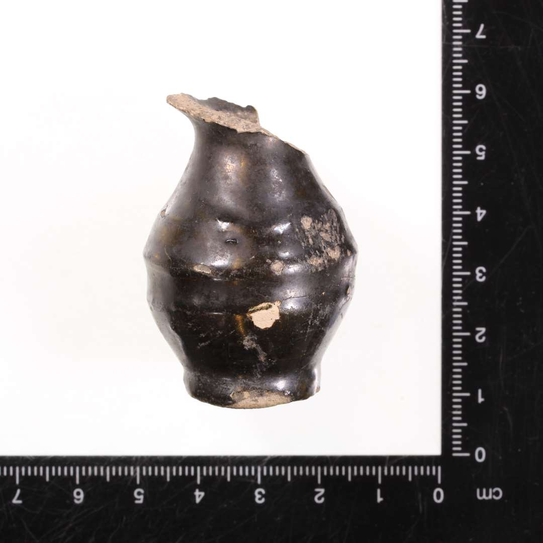 Rangle eller miniaturekrukke af brændt ler. Krukkeformet med sort glasering. Højde: 5 cm., største bredde: 3 cm.