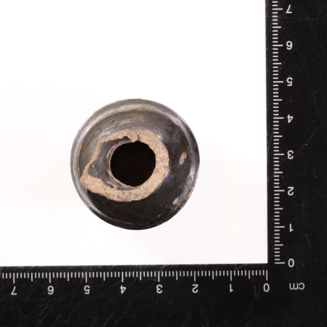 Rangle eller miniaturekrukke af brændt ler. Krukkeformet med sort glasering. Højde: 5 cm., største bredde: 3 cm.