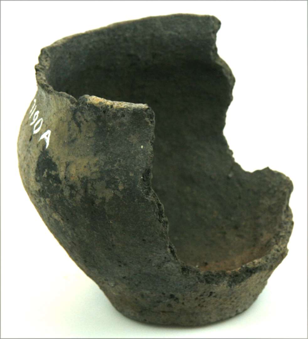 Fragment af urne med flad bund, buet side, og kort udadvendt munding. Højde: 14 cm., mundingsdiameter: 13,5 cm. Desuden tre løse skår.