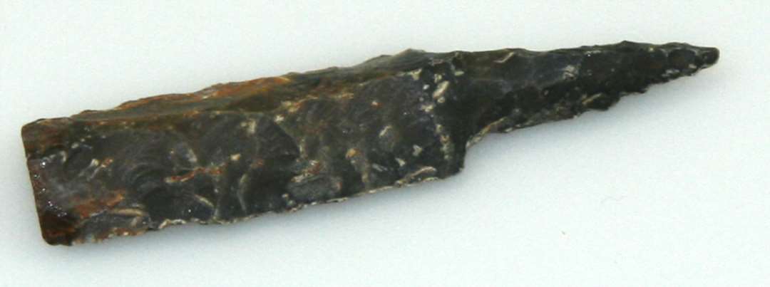 Pilespids af flint, 9x 1,5 cm, bajonetformet, tresidet m. randede ægge, grebtunge