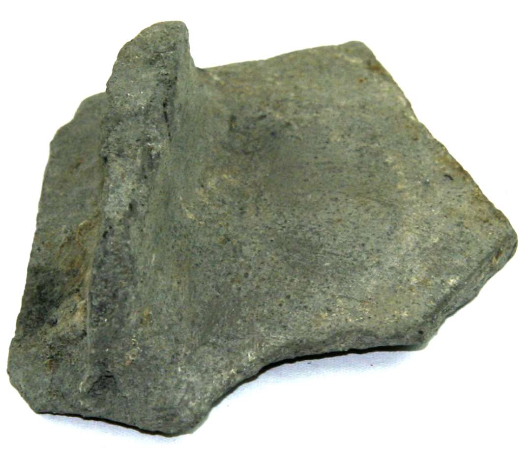 Bund eller bugskår fra gråbrændt potte. Med flad, rektangulært håndtag eller ben. Mål: 5,8 x 6,7 cm.