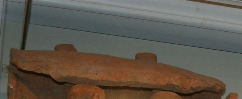 Tagsten af rødbr. Tegl med to Tappe paa den konvekse side. Længde: 50 cm. Bredde midtpaa: 22,5 cm.