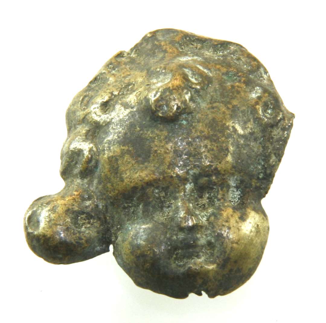 Rembeslag af bronze, formet som et lille barne/engleansigt i relief. Mål: 2,8 x 2,3 cm.