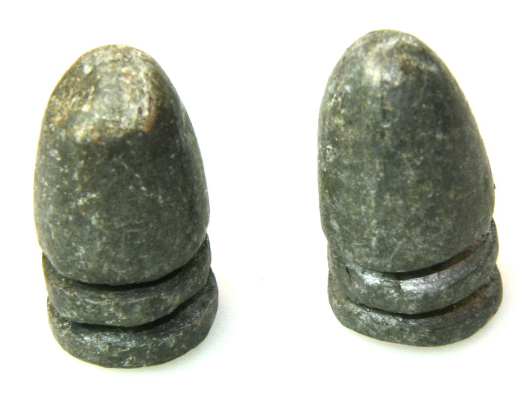 To spidskugler af bly; ved bagenden 2 dybe riller. Mål: længde 2,5 cm., diameter 1,4 cm.