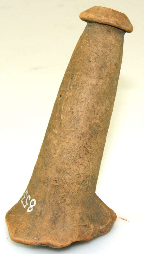 Stjert af rødbrændt lerpotte eller pande, der på indersiden har været glaseret grønligt brun. Længde 11 cm., diameter 3 cm.
