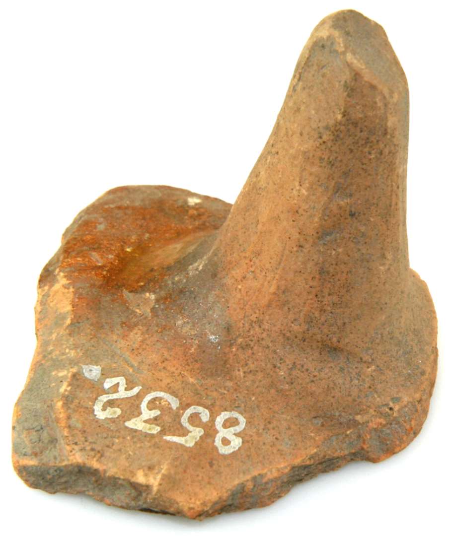 Bundskår med tå af rødbrændt lerpande, der indvendig har været brunglaseret. Mål: 7 x 5,5 cm., tåens højde 4,5 cm.