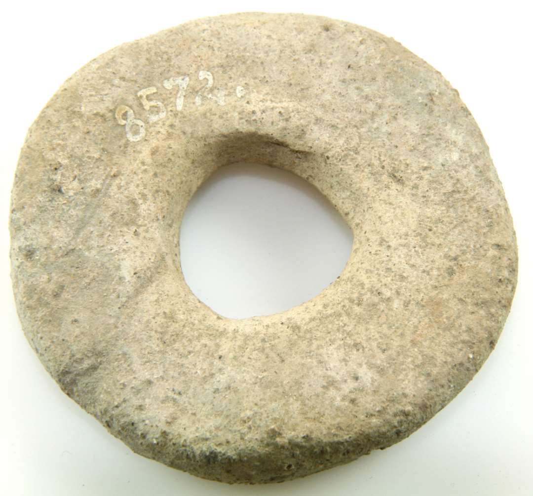 Vævevægt af hårdt, gråbrændt ler, rundt hul i midten. Diameter 8,5 cm. Tykkelse 1,8 cm. 