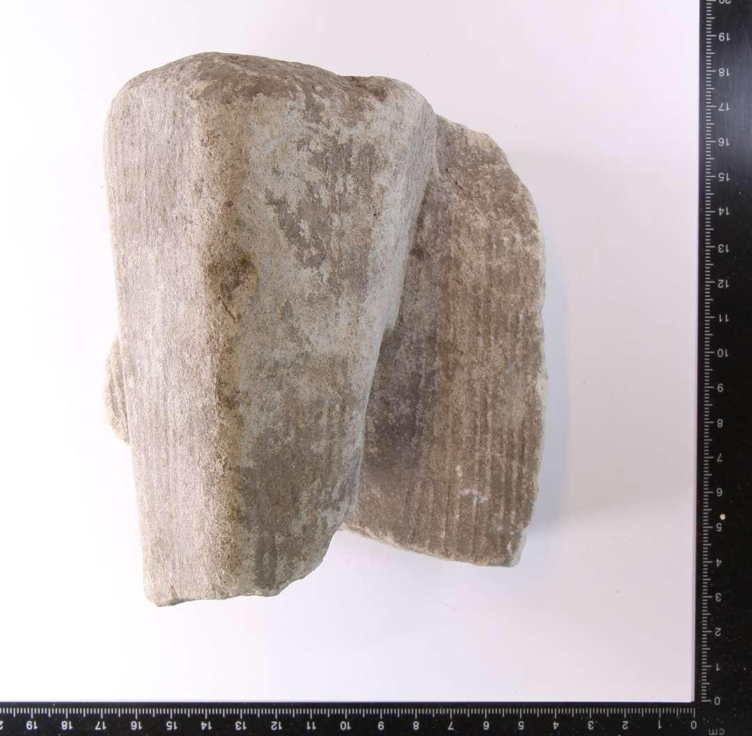 Fragment af morter af kalk-sandsten. Det nederste af hank med lidt af kummevæg. Mål: 12 x 11 x 10 cm.