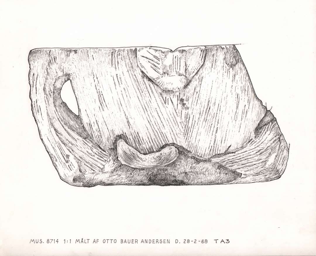 Kumme af lys kalk-sandsten; 2 ører og en tudformet udvidelse på randen. Den ene trediedel af randen og det ene øre mangler; hul i bunden. Højde 16 cm., diameter 23 cm.
