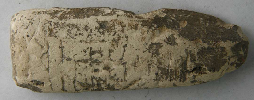 Genstand af lys ler, tilspidset. Den ene side slidt, med to parallele runeindskrifter. En anden side mindre slidt med en enkelt runeindskrift. Længde: 9 cm.