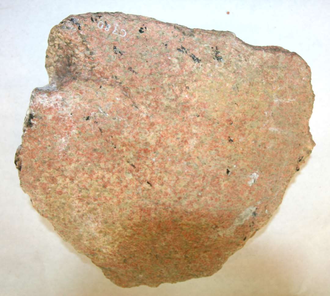 Kværnsten af rødlig granit. Uregelmæssig 5 sidig form. Rygsiden vindsleben i 3 sider. Undersiden glat. Løber? 22,5 cm. x 22,5 cm.