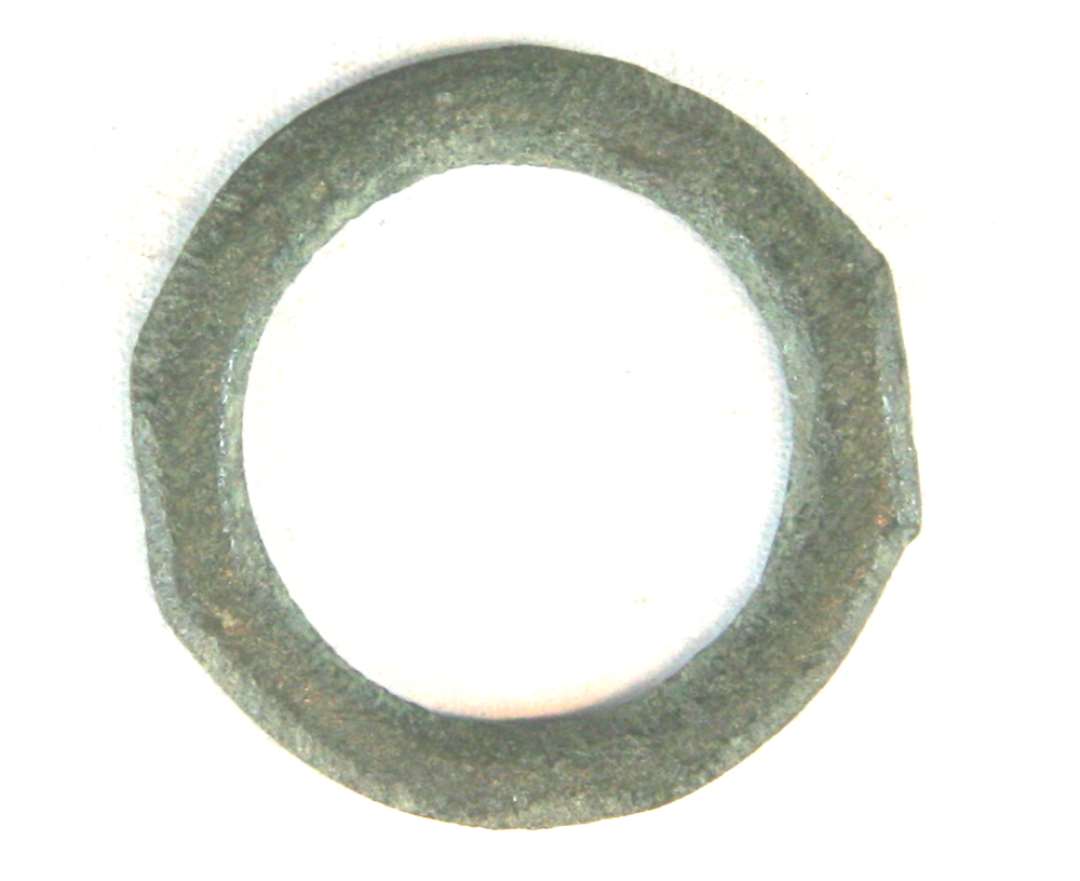 1 flad bronzering af cirkulær form med spidsovalt, svagt facetteret tværsnit. På to modstående sider af ringens yderrand er denne udtunget i et svagt fremspringende, lige afskåret parti, ca 1 cm. bredt, der giver ringen et ejendommeligt kantet udseende. Ringens ydre diameter: 3,25 cm. Ringens tykkelse: 0,25 cm.