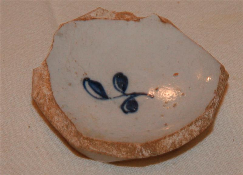 1 bundskår fra miniatureagtigt kar af fajance med ganske lav fodrand. På indersidens bund ses en blåmalet stiliseret, trebladet grenspids.