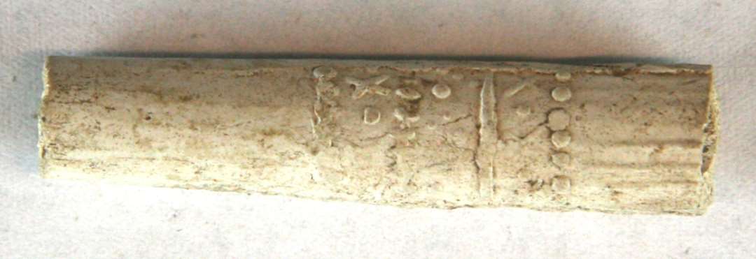1 fragment af kridtpibestilk rigt dekoreret med streger, kugler både enkelte og i rækker, samt kryds, alt i ophøjet relief. Mål: 4,5 cm.