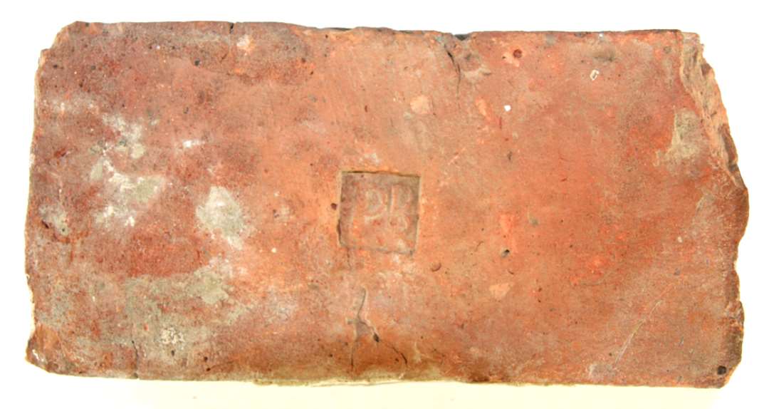 1 rødbrændt munkesten midt på hvis ene bredside der før brændingen er indpresset et stempel med glatte sider, ca. 2,7 cm. i kvadrat. I stemplet står i ophøjet relief: PB. L: 25,2 cm. Br: 12,5 cm. Tyk: 7,7 cm.