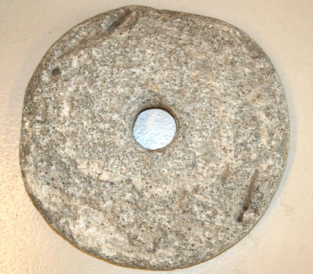 Kværnsten, cirkulær med cirkulært midterhul. Stenen storkornet granit stærkt glimmerholdigt, med tendens til spaltning. Undersiden flad, glatslidt oversiden ganske svagt hvælvet. Diameter: ca. 42 cm. Diameter af midterhul: ca. 9 cm.