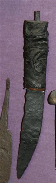 Kniv af jern Enægget. Klingen noget bøjet. Skaft af træ, forneden holdt på plads af en kobberring. Knoppen mangler. L. 22 cm. Heraf skaftet 8,5.