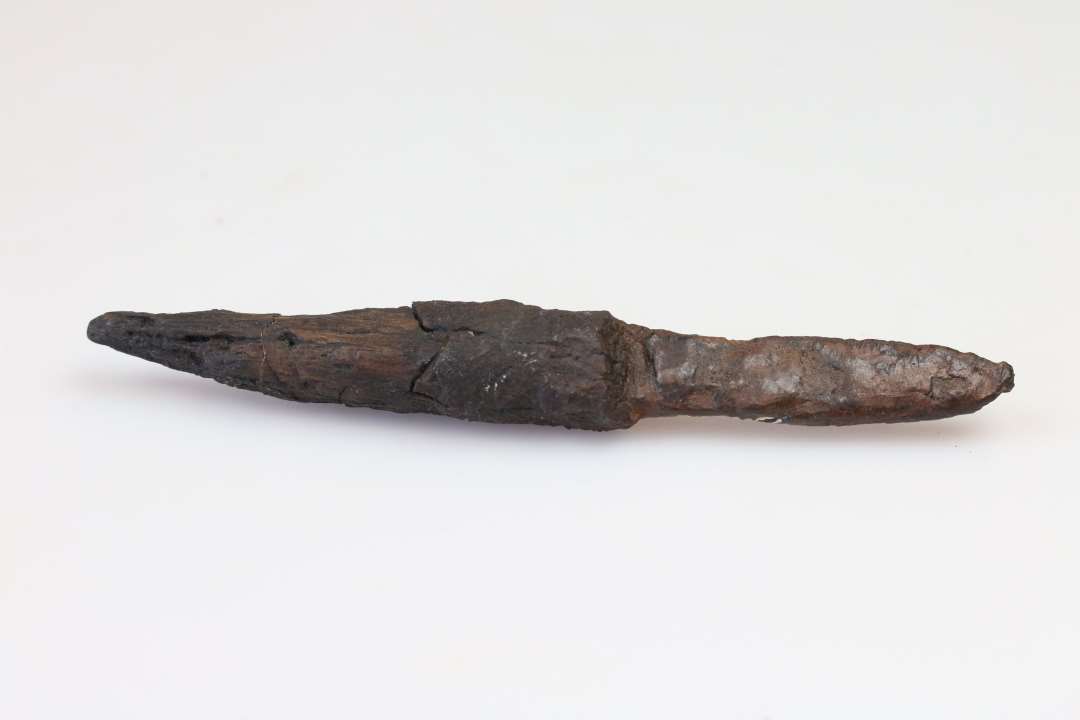 Jernkniv med skaft, fundet i forbindelse med lårbensknoglen, med skæftet skråt ind mod denne. 