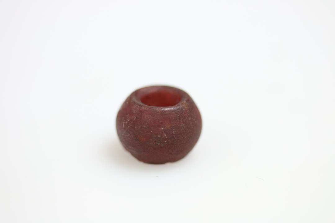 Rødlig perle, ca 1 cm i diameter, beliggende på ca 1 cm. tykt lag af sort materiale. 