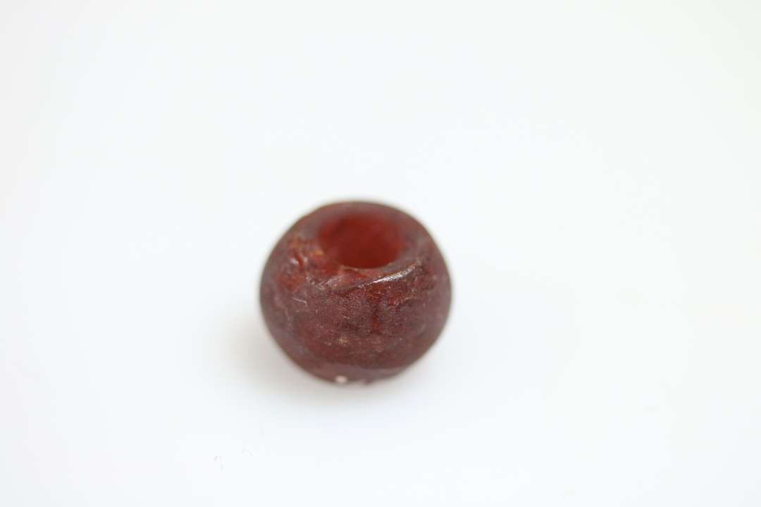 Rødlig perle, ca 1 cm i diameter, beliggende på ca 1 cm. tykt lag af sort materiale. 