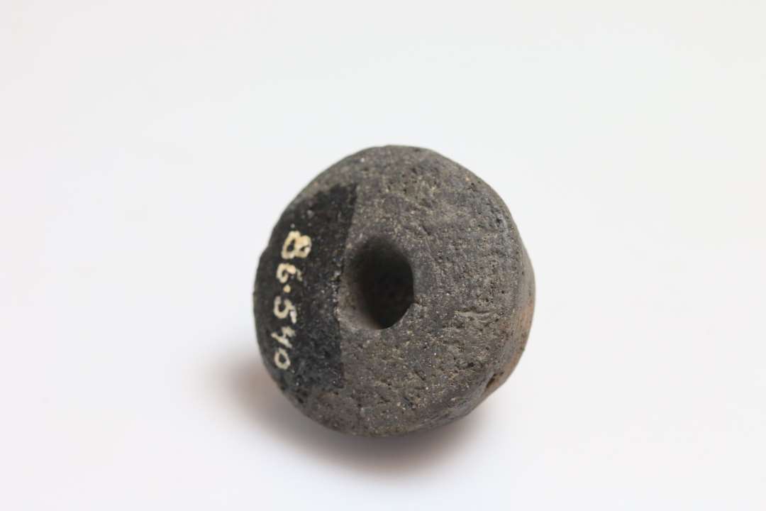 Tenvægt, med 4 svagt indridset korstegn, af brændt ler. Form: konisk rundet, bredt bund. Bredde 4 cm, højde 2,5 cm.