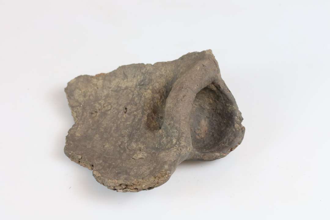 Randskår/svaleredeøre af groftmagret, brunt gods. Mål: 12 x 13 cm. Randtyk: 1,0 cm. Vægtyk: 1,0 cm.