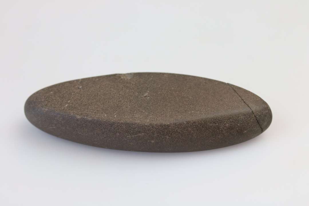 Banke/glittesten. Spidsoval form. Længde 8,0 cm. Finkornet sandsten der bærer spor af stærk brug. 