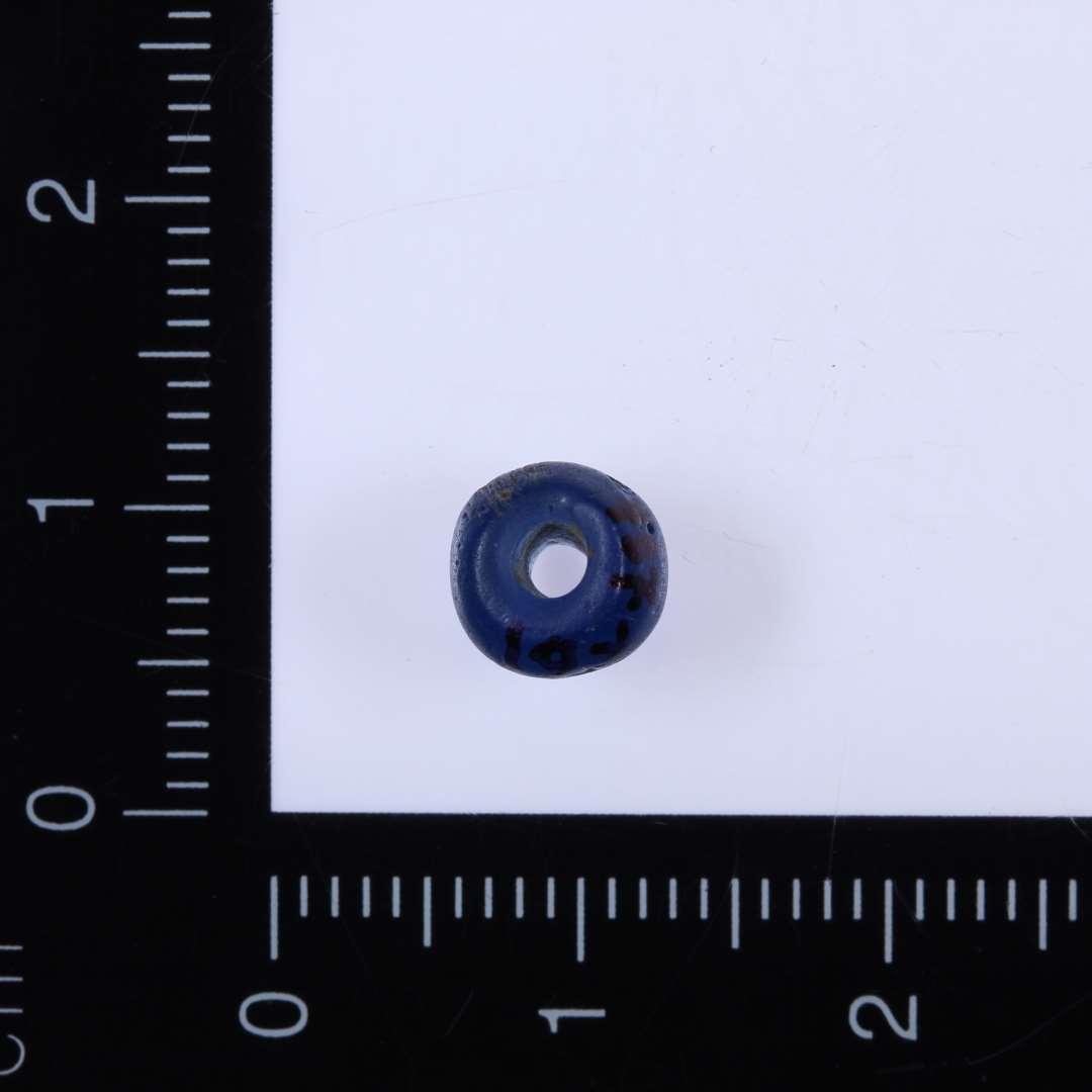 Blå perle, diameter 0,6 cm, tykkelse 0,5 cm. 