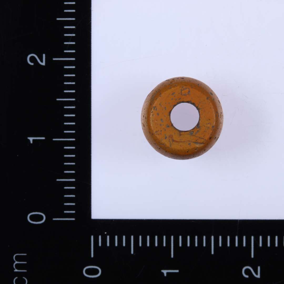 1 orange glasperle af rundet cylinderform, med lige afskåret over og underside. Diameter 1 cm, højde 0,7 cm, huldiameter 0,3 cm. 