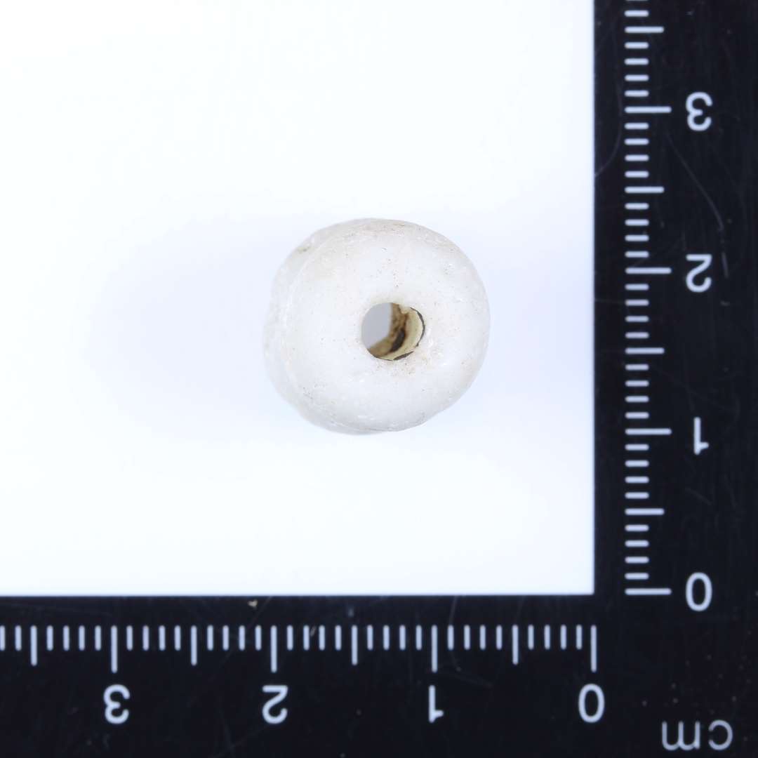 1 dobbeltperle af mælkehvidt glas. Perlen består af 2 sammensmeltede nærmest ovale enkeltperler. Ret slidt på overfladen. Diam. 1.3cm, Højde 1.3-1.5cm, Hul 0.3-0.4cm