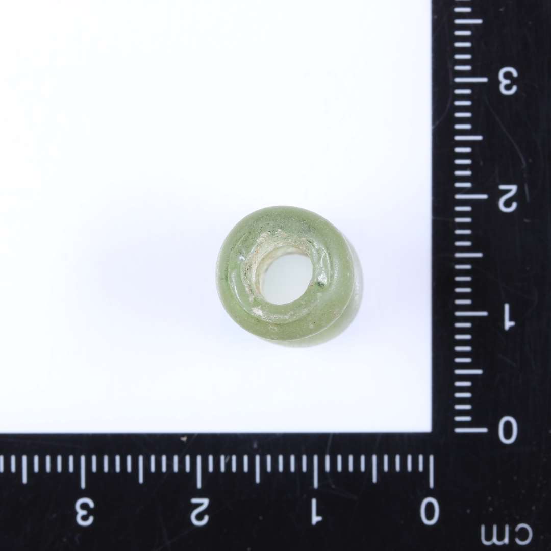 1 dobbeltperle af lyst gulgrønt klart glas. Perlen består af 2 sammensmeltede cylinderformede enkeltperler. Ret slidt på overfladen. Diam. 1.15cm Højde 1.45cm Hul 0.5cm