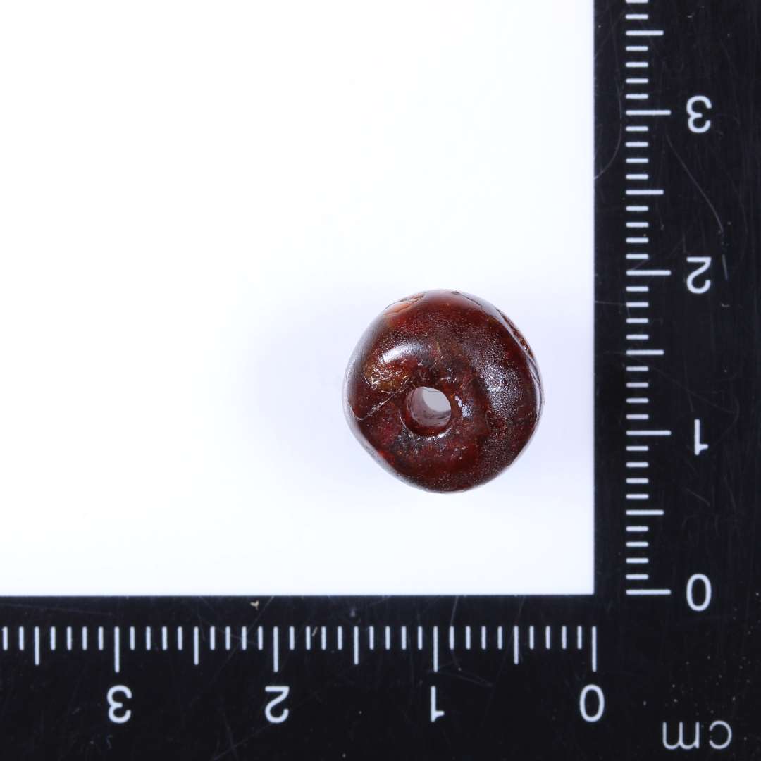 1 ravperle, afrundet cylindrisk til oval, affladede ender.  Diam. 1.2cm, højde 0.8-0.9cm, hul 0.25-3cm