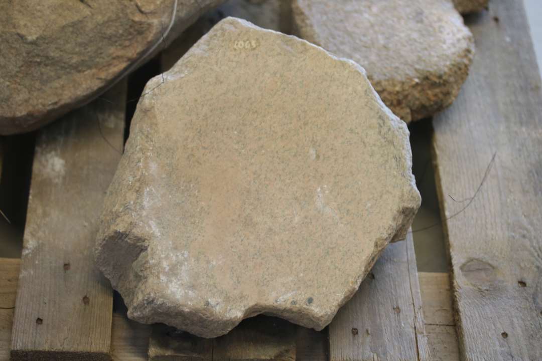 Skubbekværn, længde 35 cm,. Bredde 31 cm., tykkelse 16 cm., meget kantet, lys brunlig, finkornet grånistret granit, overfladen nedslidt 1,5 cm.