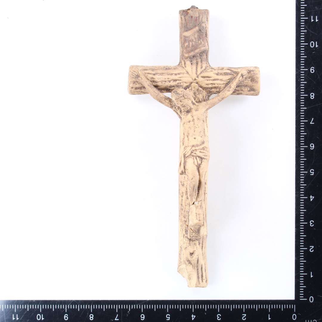 Krucifiks af ler. Længde: ca. 11 cm.. Let fragmenteret på nederste del af korset. I øverste korsarm sidder metalrester fra ophæng eller lignende.