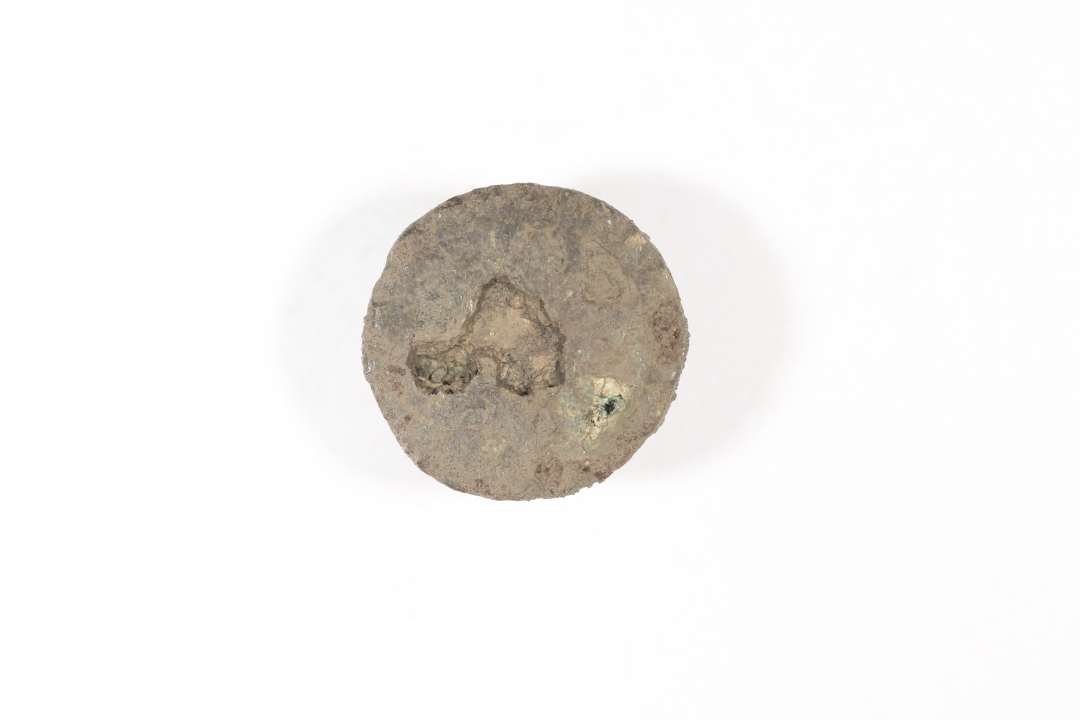 Emaljefibel. Der er tale om en cirkulær pladefibula af bronze med emaljeindlægning; muligvis korsemaljefibula. Smykket er temmelig dårligt bevaret, så mønsteret og emaljens farve kan ikke ses. Der er rester af støbt nåleanordning på bagsiden. Vikingetid eller ældre Middelalder. Diameter: 1,9 cm.