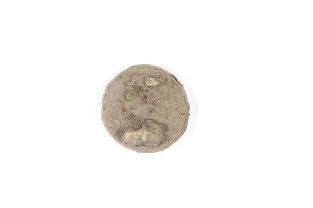 Emaljefibel. Der er tale om en cirkulær pladefibula af bronze med emaljeindlægning; muligvis korsemaljefibula. Smykket er temmelig dårligt bevaret, så mønsteret og emaljens farve kan ikke ses. Der er rester af støbt nåleanordning på bagsiden. Vikingetid eller ældre Middelalder. Diameter: 1,9 cm.