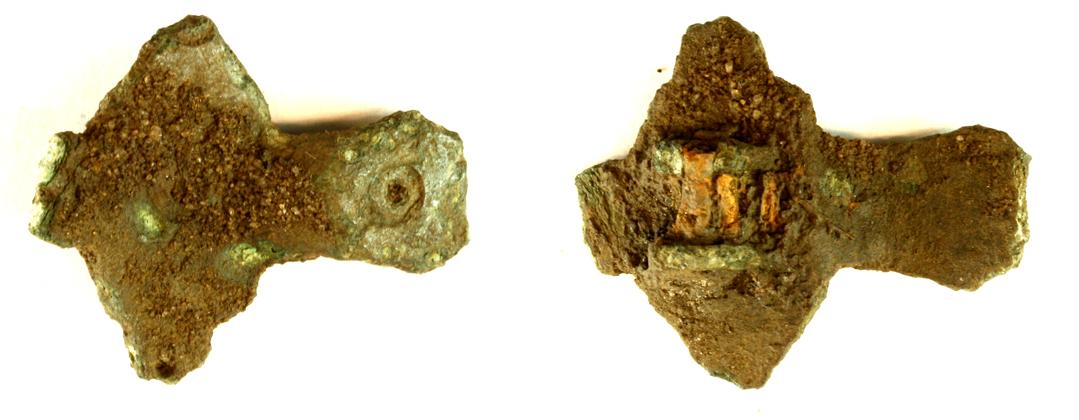 Fragment af korsformet fibel med fint bevaret nålefæste. Med punktcirkelornamentik. Mål: 25 x 30 mm