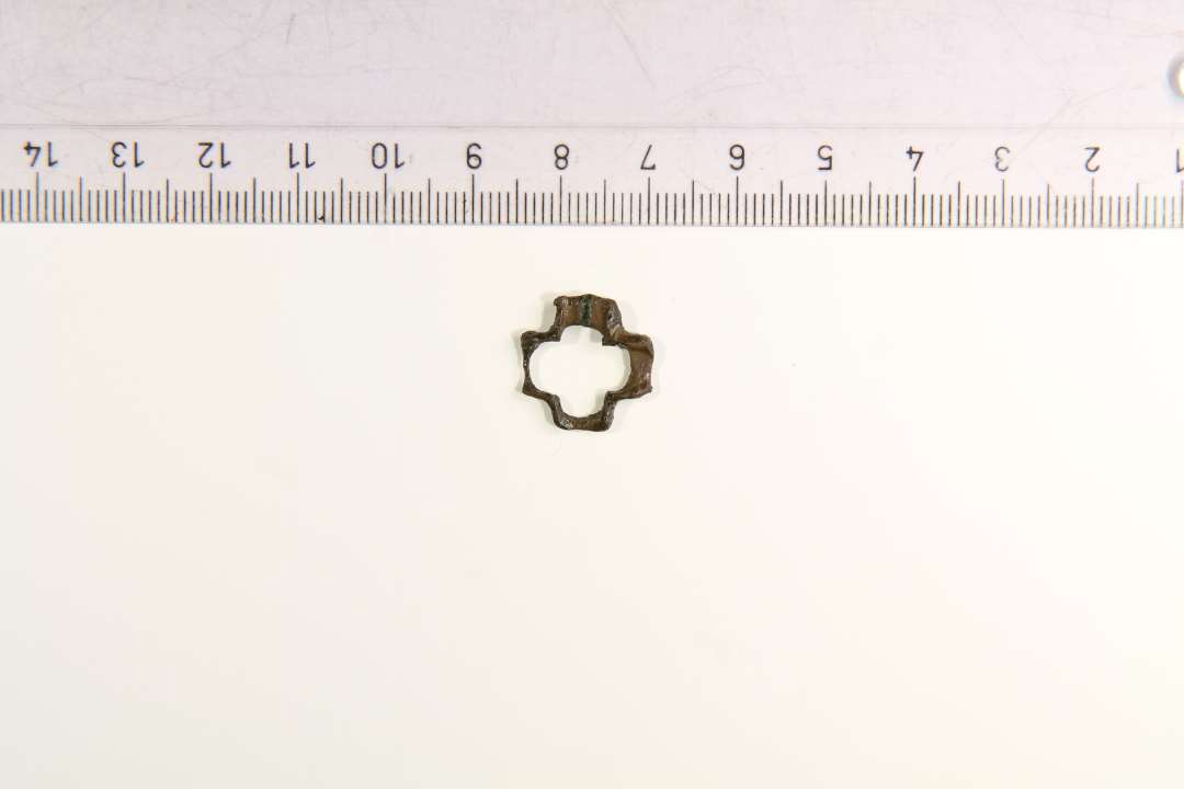 Lille korsformet beslag, antagelig et stukke rasleblik fra seletøj. I en af åbningerne synes der at være slid. Mål 15 x 15 mm
