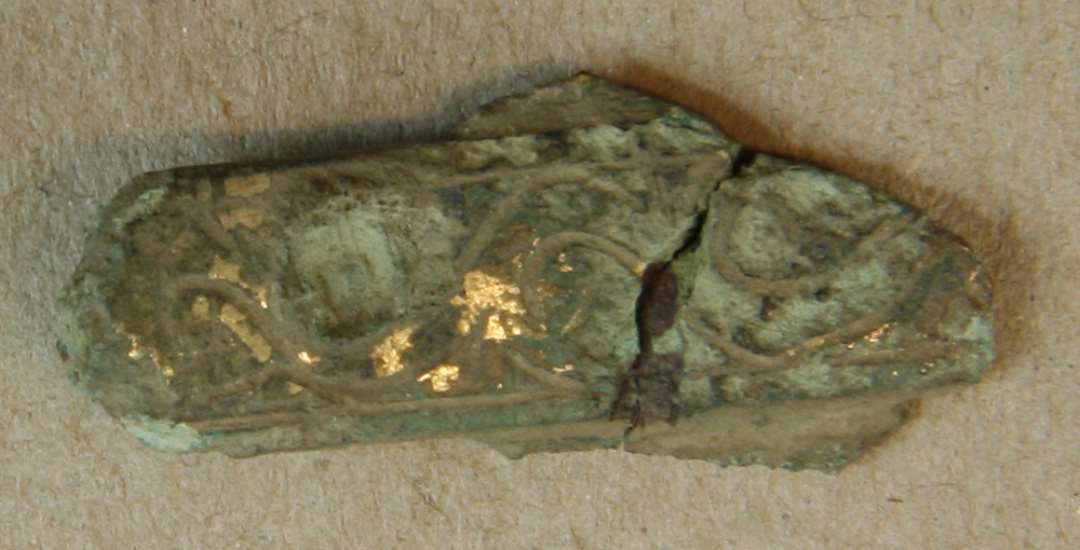 Fragment af fibel? Tungeformet med dyreslyngsornamentik, forgyldt. Længde: 29 mm.